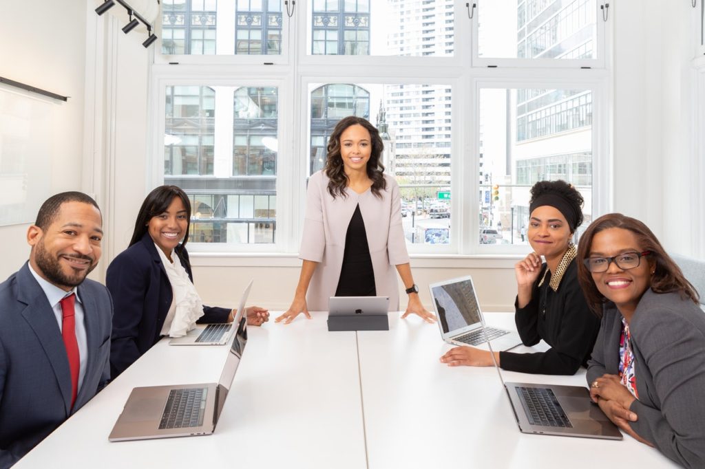 five corporate people sitting around a table carrying laptops